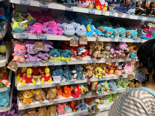 ポケモンセンターの棚いっぱいにtくさんのポケモンのぬいぐるみがならべられており、その棚の前で男の子がどれを選ぶか悩んでいる様子