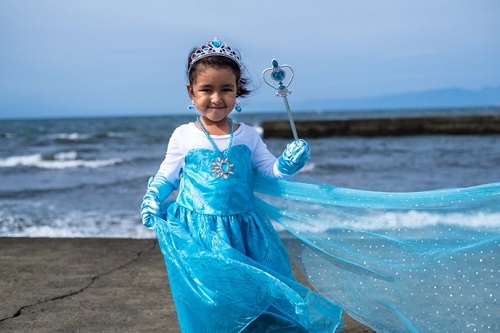 イナーヤちゃんがアナと雪の女王の水色のコスチュームを着て海岸で笑っている
