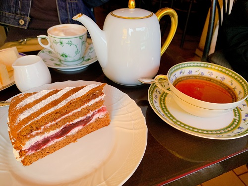 白い陶磁器のポットと紅茶が入ったカップ＆ソーサー、ケーキが載った白いお皿がテーブルに載せられている