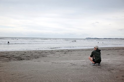 浜辺で海を眺めながら座っている佐藤さん。